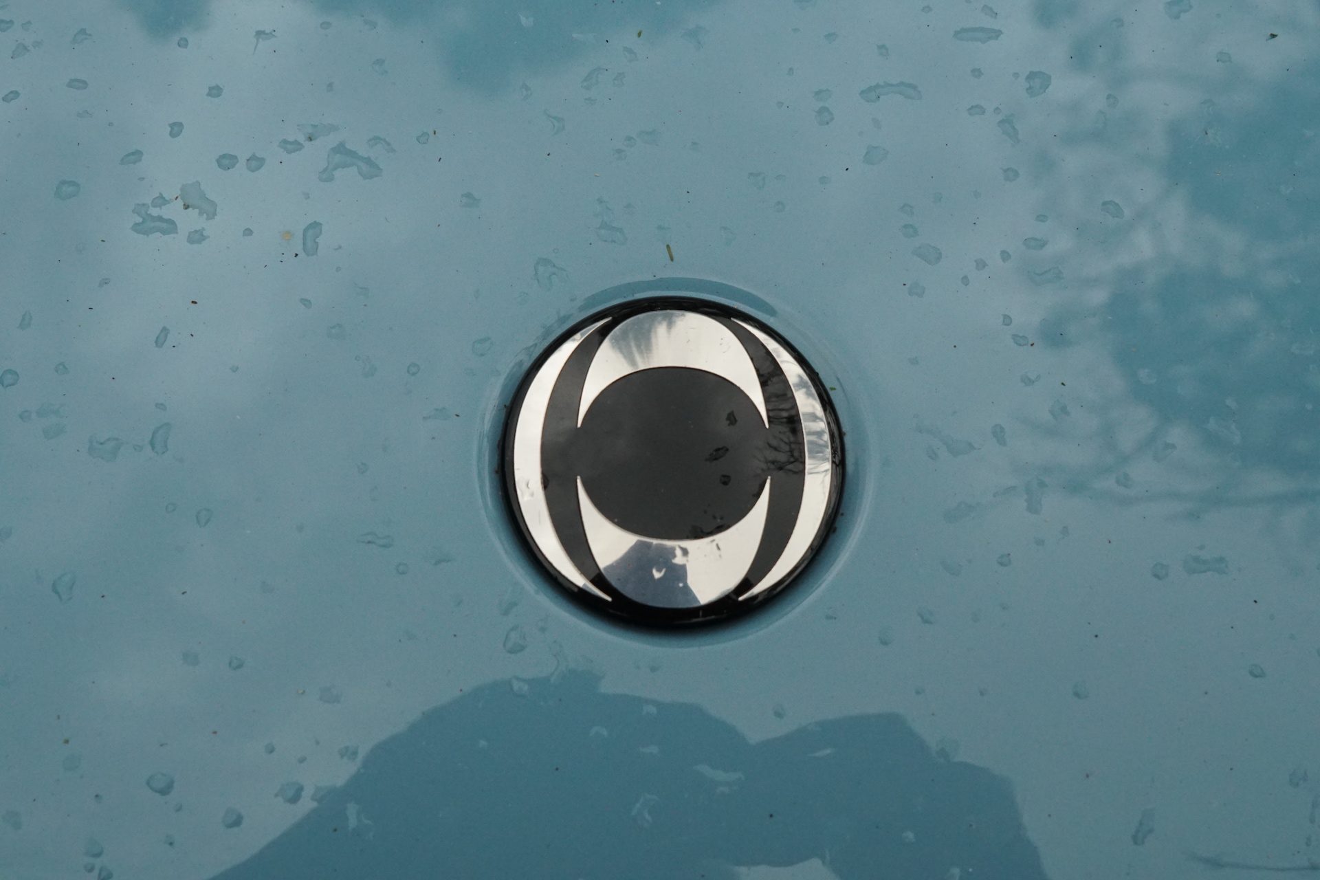Close-up of the silver and black Ineos automotive logo on the hood of a white Ineos Grenadier Trialmaster SUV.