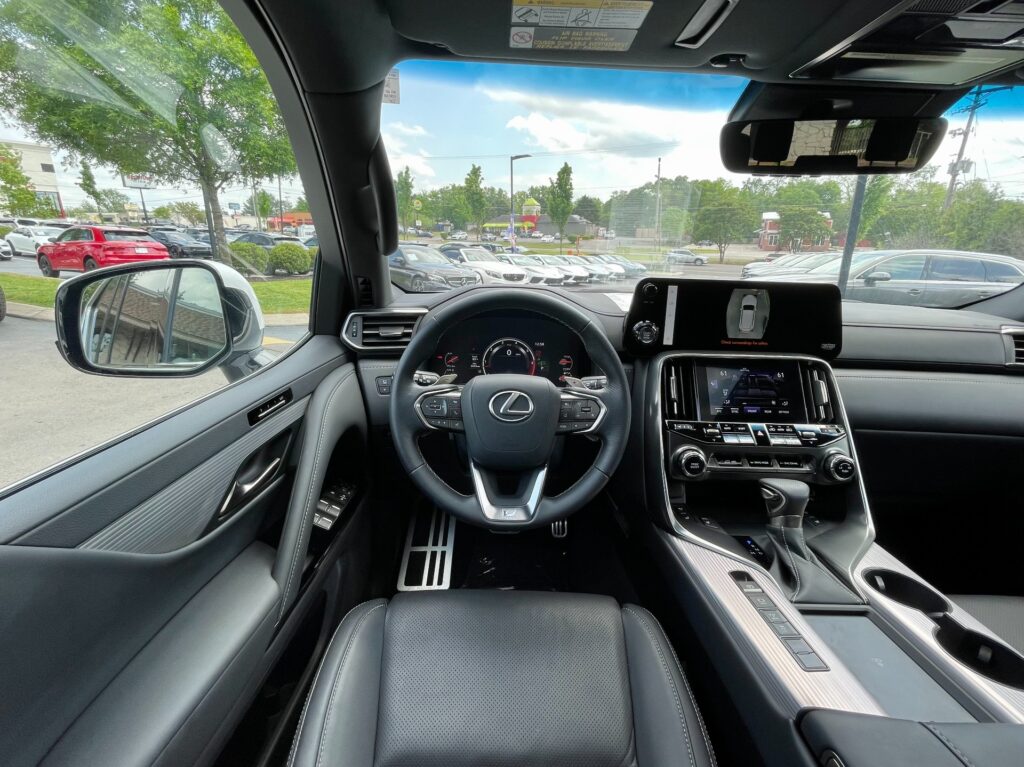 Luxurious leather interior of a white 2024 Lexus LX 600 with wood trim and panoramic sunroof, parked inside the AutoPro Nashville showroom.