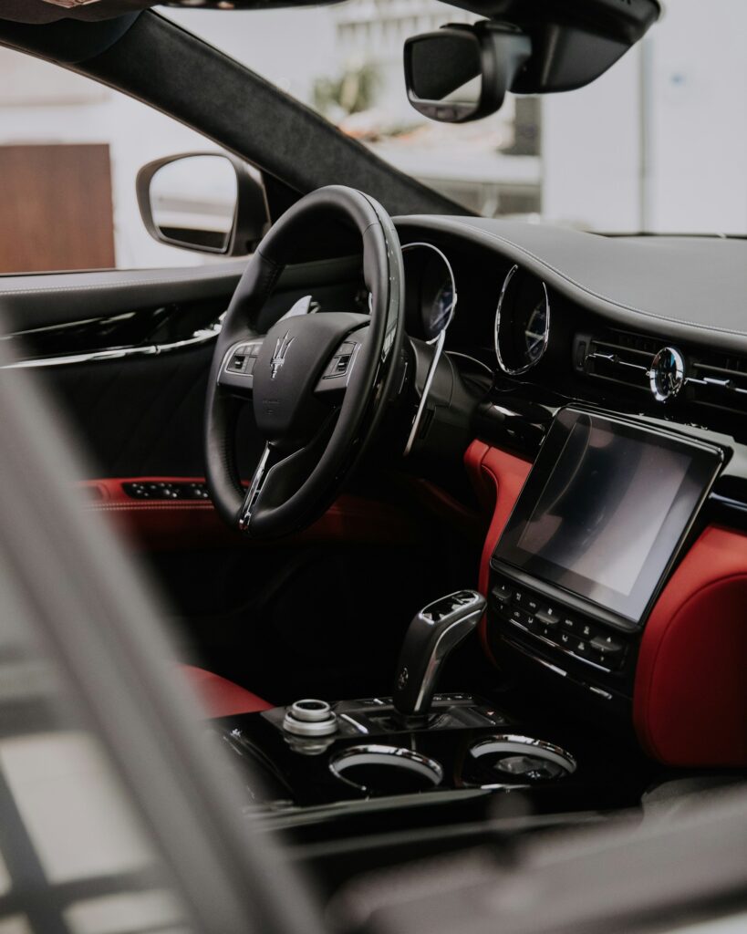 A photo of the interior of a Maserati Quattroporte, highlighting its luxurious red leather upholstery, sleek dashboard, and elegant wood accents. The photo conveys a sense of refinement and opulence, evoking the image of a high-end luxury sedan.