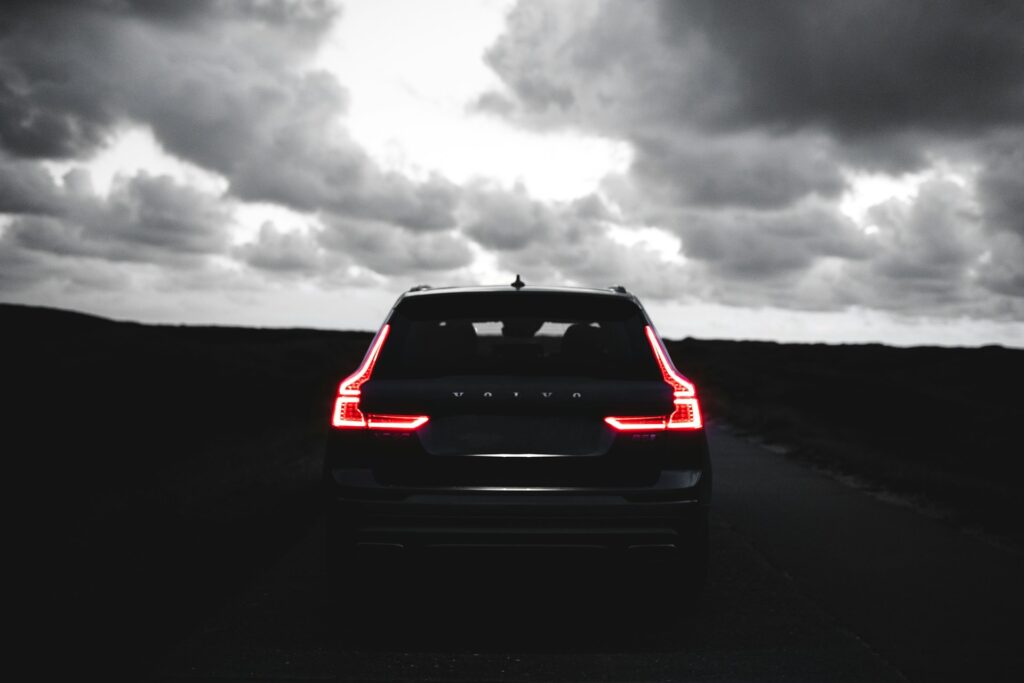 Rear view of a black Volvo XC60 SUV with its brake lights illuminated, parked on a dark road at night under cloudy skies.