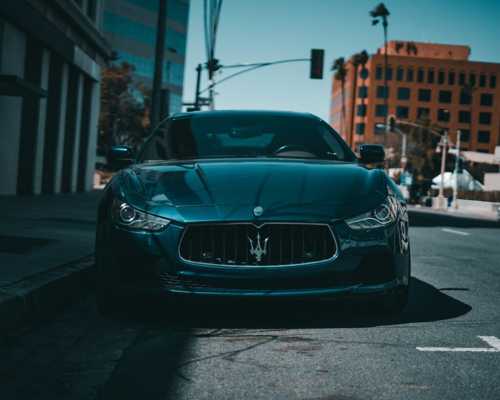 A green Maserati Ghibli luxury car parked at the side of the road in front of a tall modern building. The car's sleek design and shiny green exterior stand out against the minimalist architectural style of the building. The photo is well-composed and captures the essence of luxury and modern design.