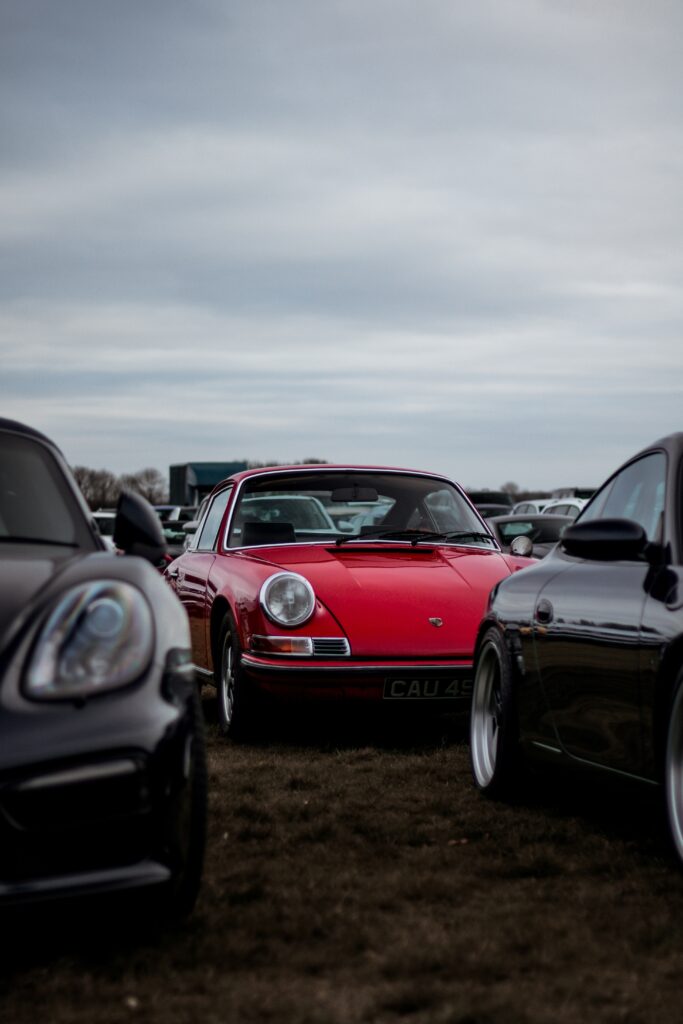 A red and black Porsche 911 parked side-by-side in a field.